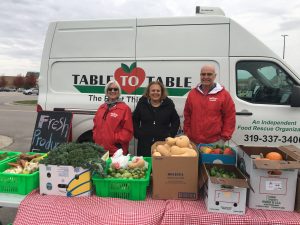 Volunteers Karen, Marnie, and Mike stand behind a table full of fresh veggies at a produce pop-up