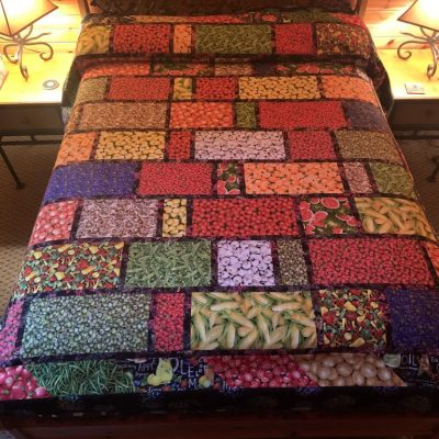 A colorful quilt featuring produce patterns displayed on a bed.