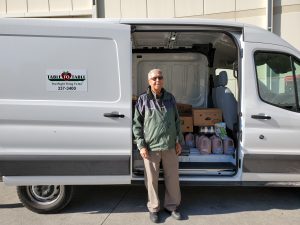 Benny stands next to the T2T van holding milk and bakery donations