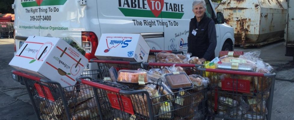 A T2T volunteer stands with four carts full of food to load into the Table to Table van