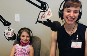 Allison and her daughter sit at the radio station studio, with microphones and headsets