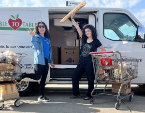 Jasmine and Cheyenne pose in front of a T2T van, with carts of bread in front of them.