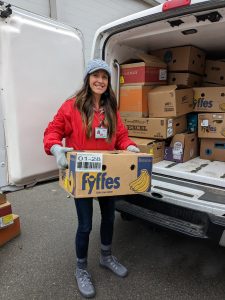 Gina stands next to an open T2T van holding a box of food