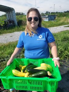 Molly stands in a farm field holding a green tote of zucchini