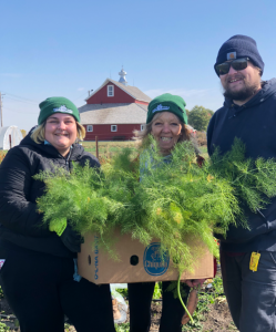 Lillian, Nora, and Alex hold a box with huge leafy greens spilling out.