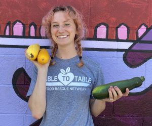 Emma stands against a purple painted mural holding yellow and green zucchini