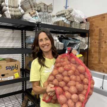 Gina holding a large sack of potatoes in the shop.